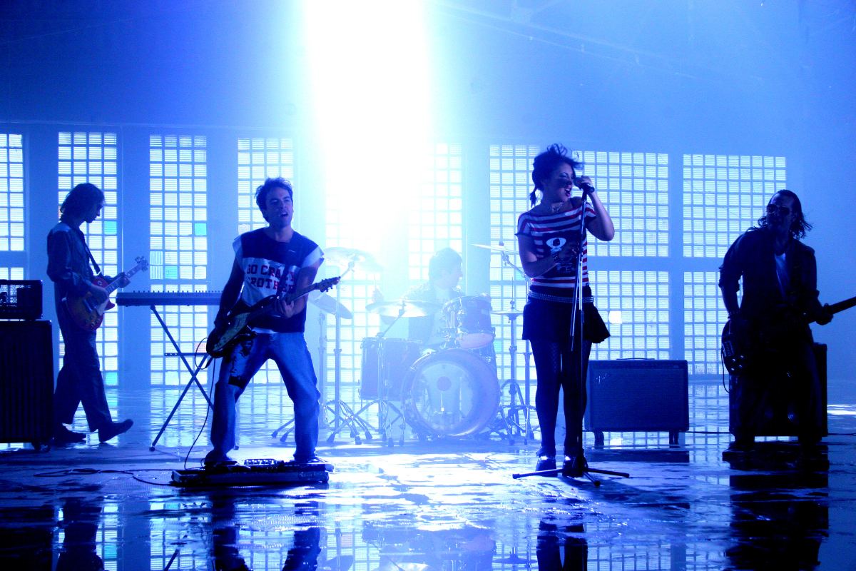 Banda en vivo sobre el escenario con luces azules, en un show con dirección musical de Marcos Rodríguez